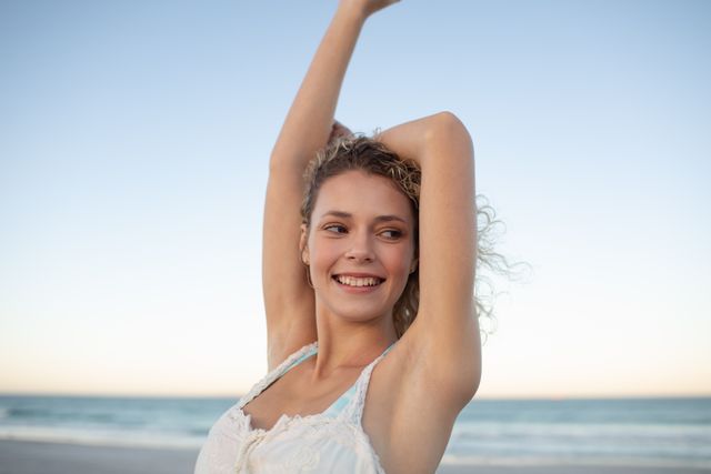 Smiling beautiful woman standing with arms up on the beach