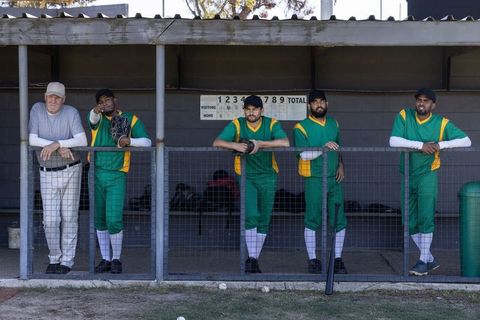 Dugout team leaning on rail watching game, baseball players and coach in green uniforms