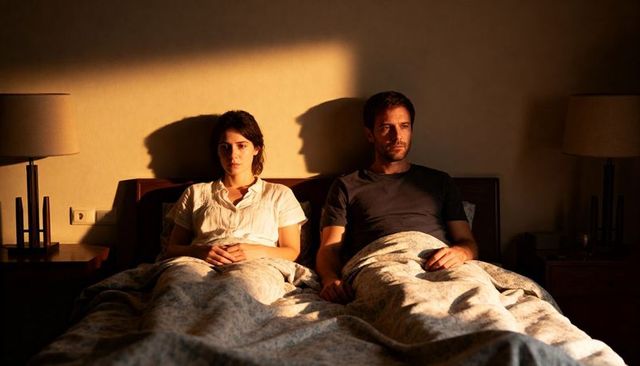 Couple lying awake in bed under warm golden light, silent tension and emotional distance