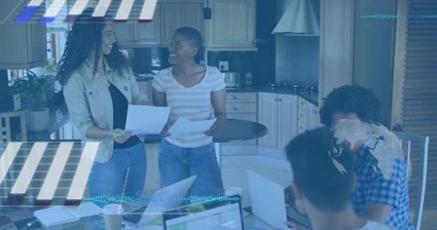 Team collaborating in casual kitchen workspace, reviewing documents and working on laptops