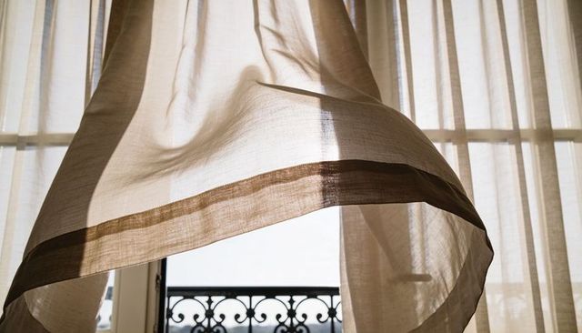 Billowing beige sheer curtain flowing over balcony railing, soft sunlight filtering