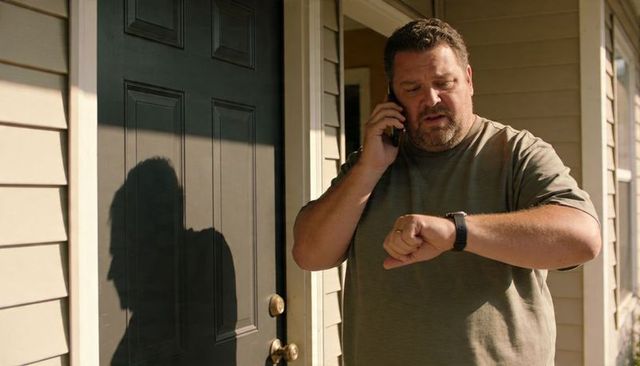 Bearded man checking smartwatch while talking on phone on sunlit front porch