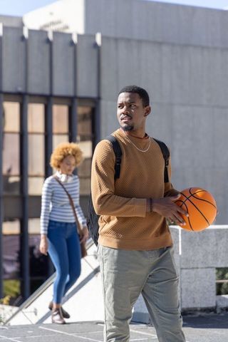 African american man holding basketball on urban campus plaza, casual student lifestyle