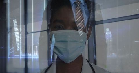 Black doctor standing by window wearing face mask and stethoscope with city reflection