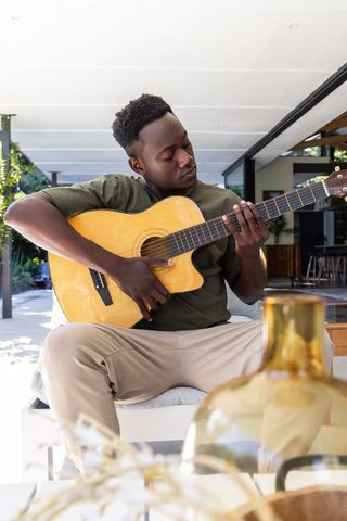 Adult african man playing acoustic guitar on modern patio veranda relaxed musician