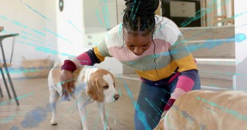 Kneeling woman petting beagle and tan dog in colorful striped sweater at home