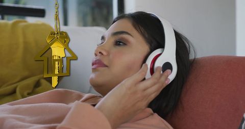 Woman relaxing with headphones beside golden house key symbol