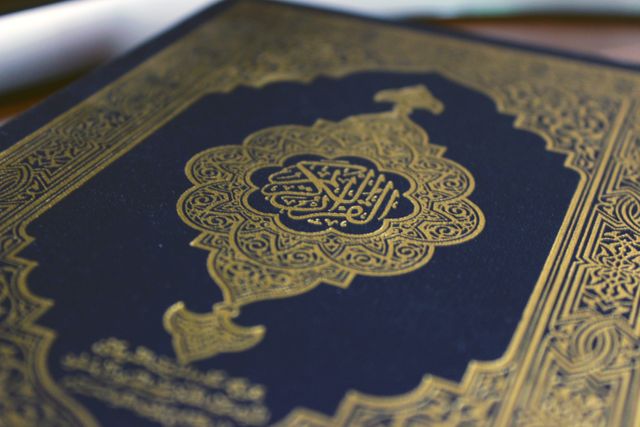 Close-up of Quran cover featuring intricate Arabic calligraphy and a beautiful gold ornate design. Ideal for content related to Islamic religion, spirituality, and religious studies. Useful for websites, articles, and educational material highlighting Islamic culture and heritage.