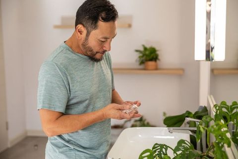 Mature asian man applying facial serum at bathroom sink with plants, minimalist vanity