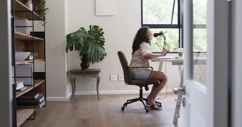 African american woman recording podcast at minimalist desk with laptop and microphone