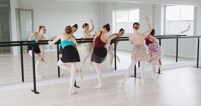 Ballerinas are practicing dance poses in a brightly lit ballet studio with mirrors. All dancers wear ballet attire including leotards, skirts, and pointe shoes. This image can be used for advertising dance schools, promoting ballet classes, illustrating exercise and fitness concepts, providing visuals for articles on classical dance, or for use by educational materials on ballet and performing arts.