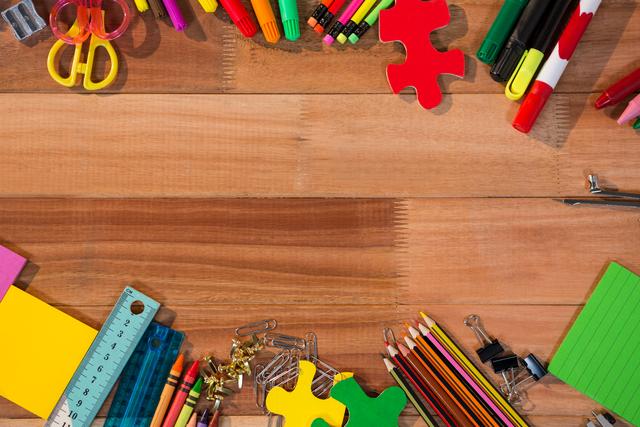 Various stationery items including pencils, pens, markers, scissors, paper clips, and a ruler are arranged on a wooden table. This image is ideal for use in educational materials, back-to-school promotions, office supply advertisements, and creative workspace inspiration.