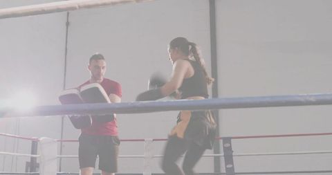 Boxing coach training female boxer with focus pads in gym ring