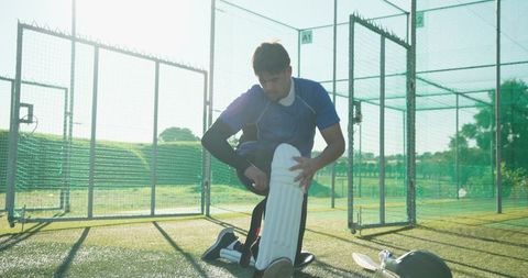 Kneeling cricketer securing batting pad in practice nets during sunny outdoor training