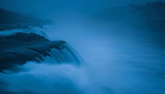 Cascading waterfall at twilight casting blue mist over rocky river gorge long exposure