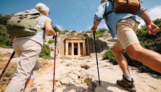 Active senior couple hiking to ancient rock-cut temple with trekking poles and backpacks