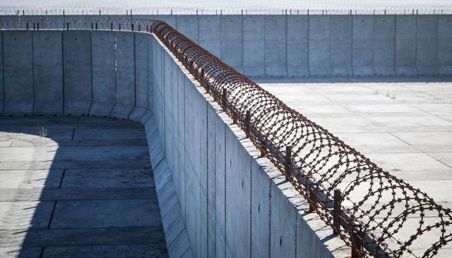 Rusted concertina wire topping tall concrete wall emphasizing perimeter security and isolation
