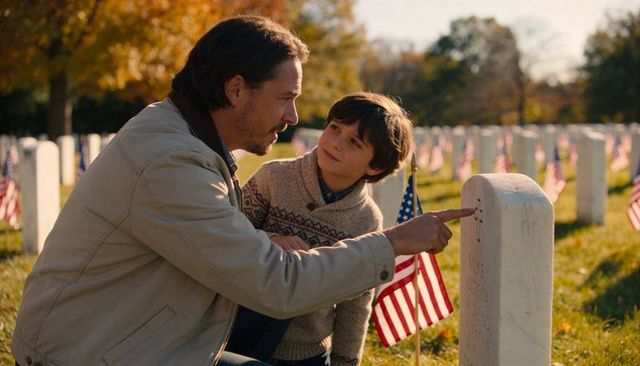 Father kneeling with son pointing at veteran headstone among american flags on autumn day