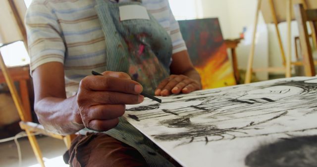 Person drawing with charcoal showcasing artistic talent in an art studio. The artist's hands are focused on creating a detailed sketch. Useful for topics related to creativity, art education, artistic techniques, and creative professions.