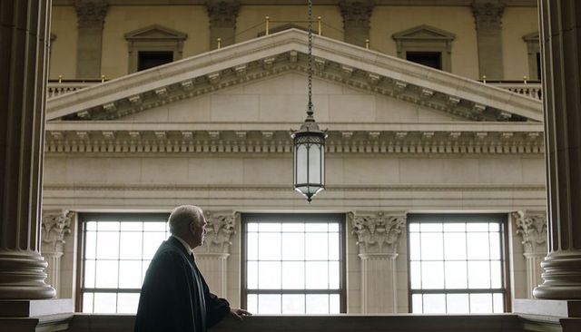 Standing senior judge leaning on stone balustrade in neoclassical courthouse gallery