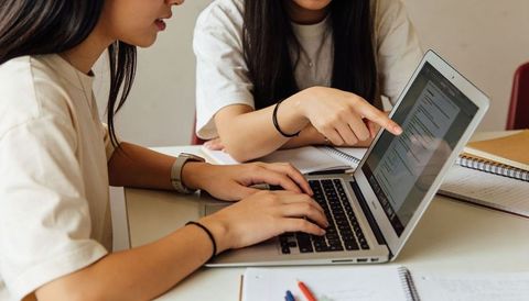 Teenage Asian Students Collaborating on Laptop While Taking Notes Closeup Study Session