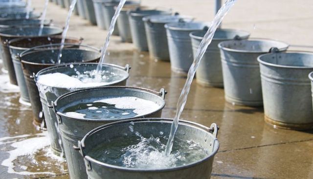 Filling galvanized buckets with flowing water on sunlit concrete, creating splashes