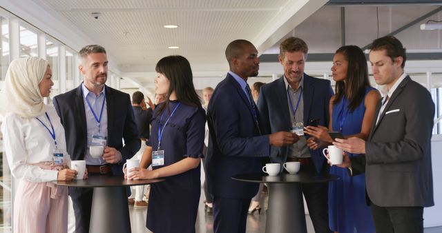 Image depicts business professionals from diverse backgrounds interacting and networking during a coffee break at a business meeting or conference. Ideal for use in articles, marketing materials, and social media posts about corporate events, professional networking, and business collaboration.