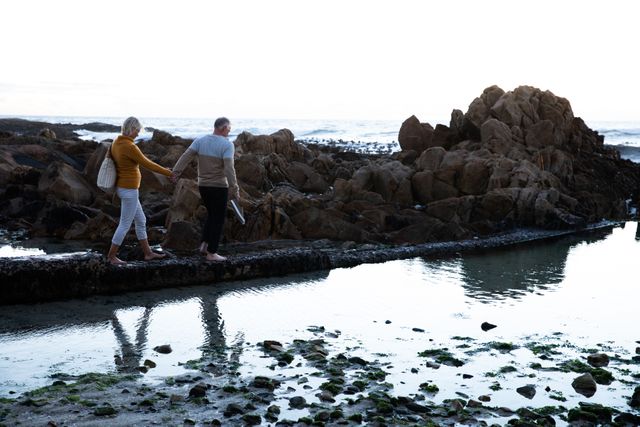 Senior couple walking on rocky seashore holding hands - Download Free Stock Photos Pikwizard.com