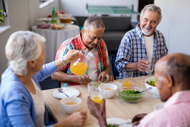 Group of senior friends enjoying breakfast together in a nursing home. They are smiling and engaging in conversation, creating a warm and friendly atmosphere. This image can be used to depict senior living, community bonding, and the importance of social interactions among the elderly. Ideal for use in healthcare, retirement home promotions, and articles on senior well-being.