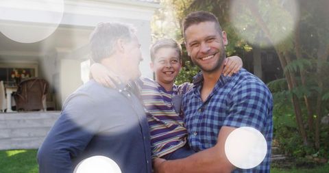 Three-generation family smiling on front porch with sunlit lens flare and warm embrace