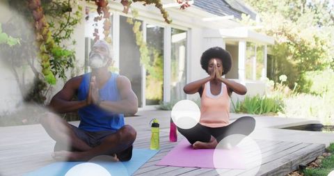 Couple practicing outdoor morning yoga on backyard deck meditating with water bottles