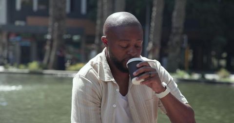 African american man enjoying takeaway coffee by urban plaza pond on sunny summer day