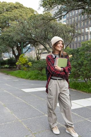 Young female college student smiling on urban campus walkway holding notebooks and backpack