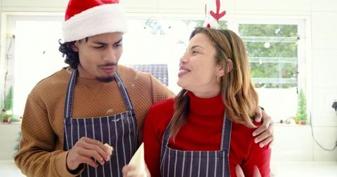 Couple decorating holiday cookies in matching striped aprons in sunlit kitchen