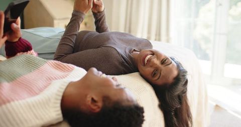 Happy Couple Relaxing on Bed While Using Smartphones