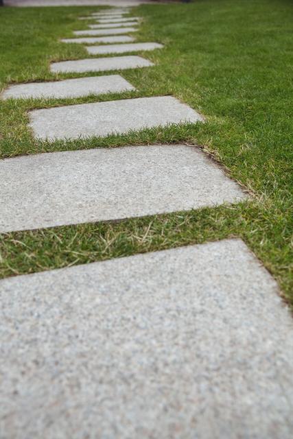 This image shows a cement walkway with stepping stones in a garden surrounded by green grass. Ideal for use in landscaping brochures, garden design inspiration, outdoor living blogs, and home improvement websites.