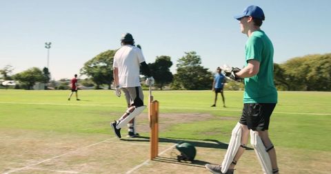 Wicketkeeper catching ball while teammates playing casual cricket match in sunny park
