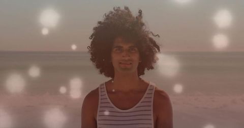 Curly-haired young man standing on sunlit beach at golden hour with dreamy bokeh