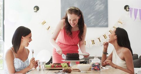 Female Friends Celebrating Birthday Cutting Cake in Dining Room