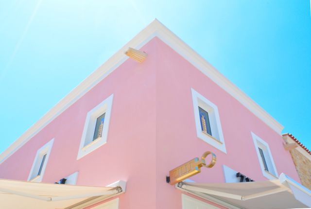 Modern pink building depicting minimalist architecture with sunlit facade. Bright blue sky enhances the vividness of the structure. Ideal for use in architectural reviews, cityscape promotion materials, and urban design blogs.
