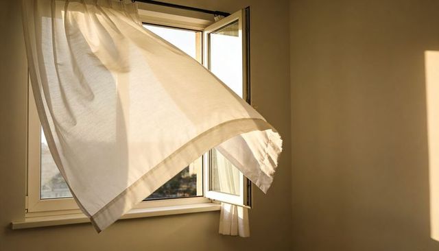 Sunlit sheer curtain billowing through open window casting warm sunbeam in minimal bedroom
