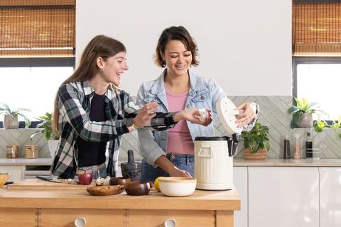 Diverse friends preparing dinner at wooden kitchen island with compost pail and bright light