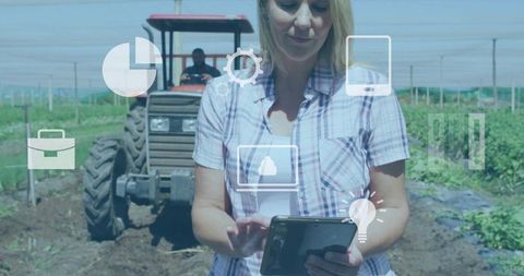 Female farmer using tablet with agritech dashboard and tractor in field
