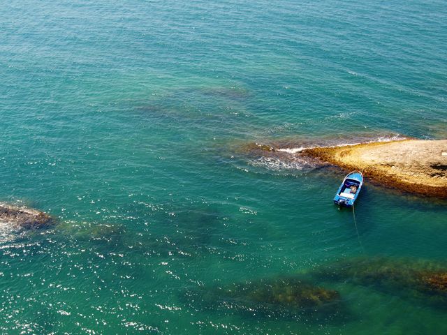Small blue boat anchored in turquoise waters next to a rocky shoreline. Ideal for concepts of solitude, adventure, travel, and natural beauty. Perfect for tourism promotions, outdoor activity advertisements, and inspirational blogs centered on ocean views.