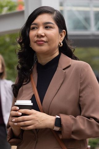 Professional woman holding coffee cup wearing smartwatch and brown blazer in urban plaza