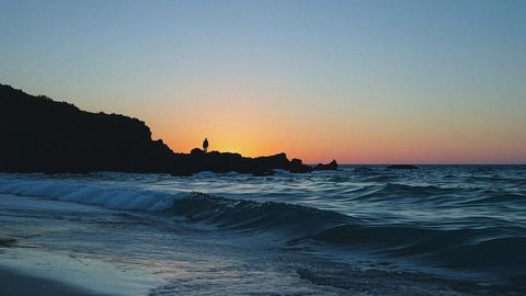 Silhouette of Man Observing Sunset Over Ocean Waves