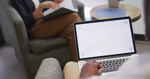 Typing on laptop with blank screen while colleague reviewing documents in office lounge