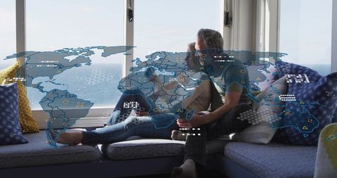 Couple relaxing on window seat with ocean view and augmented reality world map overlay