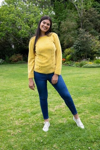 Woman relaxing in garden wearing yellow sweater and blue jeans