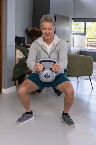 Senior Man Performing Kettlebell Squat in Modern Living Room